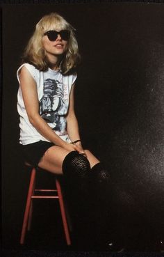 a woman sitting on top of a red stool wearing black tights and sunglasses with her legs crossed