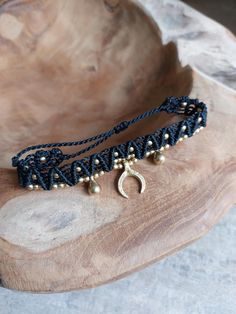 a black string bracelet with gold beads and a crescent charm on the end is sitting on a wooden surface