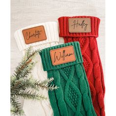 three christmas stockings with name tags on them sitting next to a pine branch and evergreen