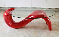 a glass table with red curved legs and a glass top on the floor in front of a white wall