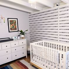 a white crib and dresser in a room with a patterned wallpaper on the wall