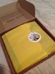 an open box with a yellow cloth and a bee sticker on the lid, sitting on a bed