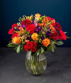 a vase filled with red, orange and purple flowers on top of a gray table