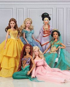 barbie dolls are sitting on the floor with their dresses and tiaras in front of them