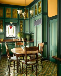 a dining room with green walls and tile flooring is pictured in this image, there are wooden chairs around the table