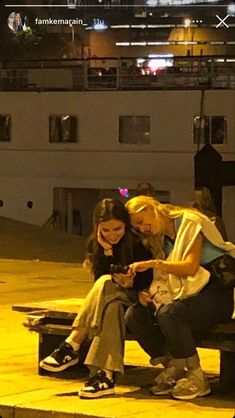 two women sitting on a bench looking at a cell phone while another woman sits next to her