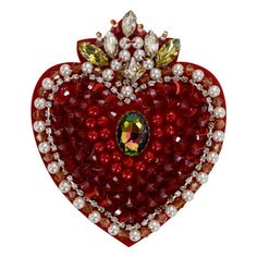 a red heart shaped brooch with pearls on it's sides and a jewel in the center