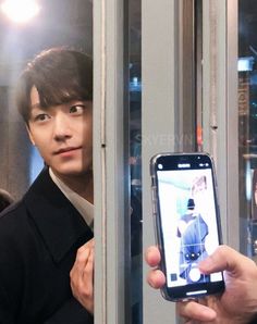 a man holding up his cell phone to take a selfie with another person in the background