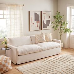 a living room with white couches and two pictures on the wall above them in front of a window