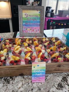 a tray filled with fruit sitting on top of a counter next to a framed sign