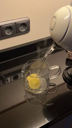 a pitcher pouring water into a glass mug with lemon wedges on the side and black countertop