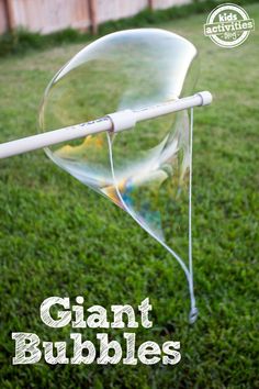 the giant bubble is being held up by a plastic stick on top of green grass