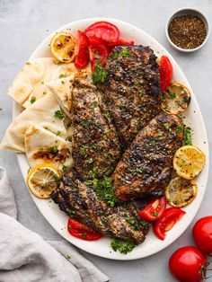 grilled fish with tomatoes, lemons and herbs on a white plate next to pita bread