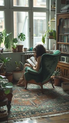 a woman sitting in a green chair next to a window with potted plants on it