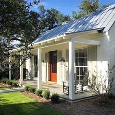 a small white house with a red door and two rocking chairs on the front porch