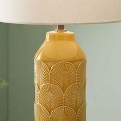 a yellow lamp sitting on top of a table next to a green wall and plant