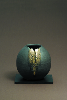 a green vase sitting on top of a wooden table next to a black stand with a gold design