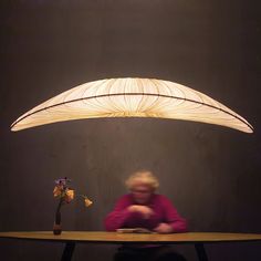 a person sitting at a table with a lamp on it and flowers in front of them