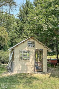 a small shed sitting in the middle of a field next to some trees and grass