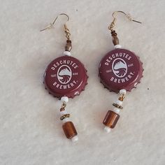 two bottle caps with beads hanging from them on snow covered ground, one is red and the other is brown