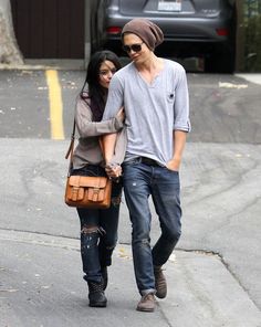 a young man and woman walking down the street holding hands with an orange handbag