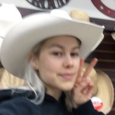 a woman with white hair wearing a cowboy hat and making the peace sign in front of her