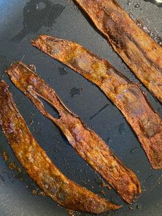 two strips of bacon cooking in a frying pan