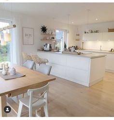 an open kitchen and dining room with wood floors, white cabinets and wooden table in the center