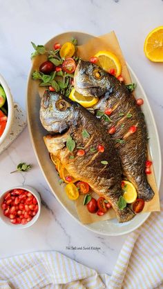 two fish on a platter with tomatoes, lemons and cherry tomatoes next to it