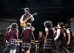 a group of young people standing on top of a stage next to an adult guitar player