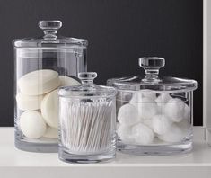 three glass containers with white cotton swabs in them on a countertop next to each other