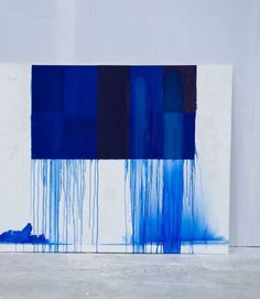 an abstract painting with blue and black squares on the bottom, in front of a white wall