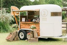 an old fashioned food truck is parked in the grass with flowers on it's side