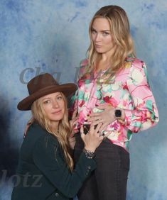 two beautiful women standing next to each other in front of a blue background wearing hats