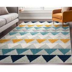 an area rug with blue, yellow and grey colors on the floor in front of a couch