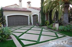 a house with grass in front of it and palm trees around the driveway area on either side