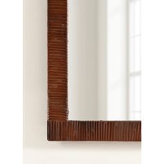 a wooden mirror hanging on the wall next to a white wall with a window behind it