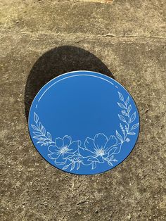 a blue plate with white flowers and leaves on it is sitting on the ground next to a sidewalk