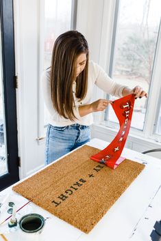 a woman is making a welcome mat with red ribbon on top of the doormat