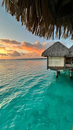 the water is crystal blue and there are two huts in the water with thatched roofs