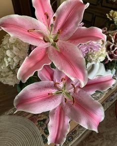 pink lilies are in a vase on a table next to white hydrangeas