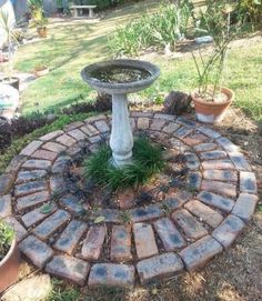 a bird bath sitting on top of a brick circle in the middle of a garden