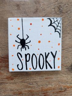 a wooden sign that says spooky with a spider hanging from it's side