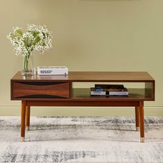 a coffee table with flowers and books on it in front of a beige painted wall