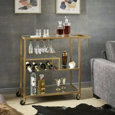 a gold bar cart with wine glasses and bottles on it in front of a gray wall