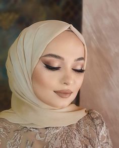 a woman wearing a hijab and makeup looks down at her eyeliners