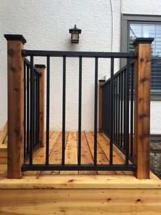 a wooden deck with black iron railings next to a white wall and window in the background