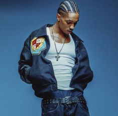 a young man with dreadlocks standing in front of a blue background wearing a jacket and jeans