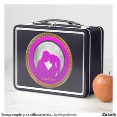 a lunch box with an image of a kissing couple on the front and side, next to an apple