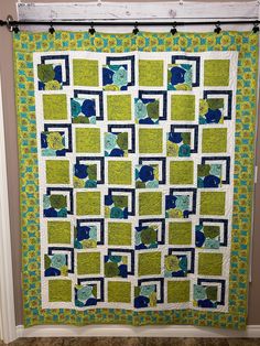 a green and blue quilt hanging on the wall